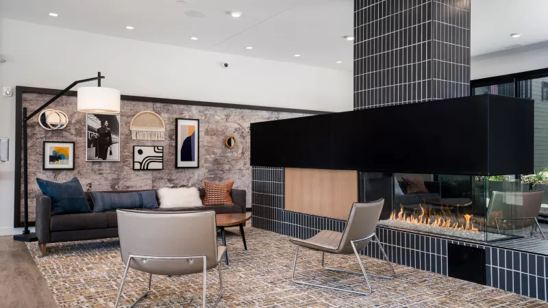 Stylish modern lounge featuring a gray sofa, abstract art, and a sleek black-tiled fireplace with glowing gas flames.