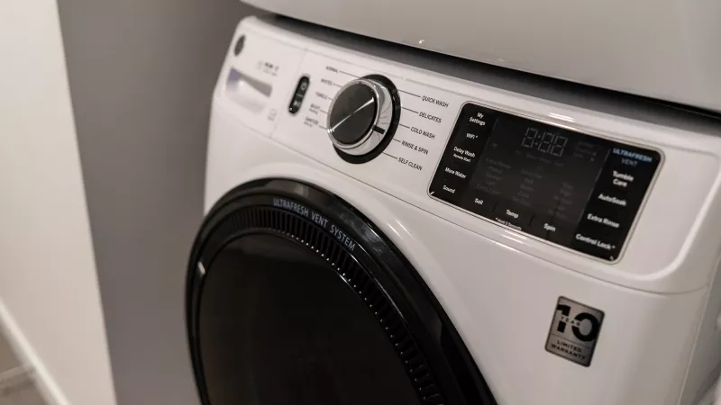 White GE front-load washing machine, stacked, with control panel, digital display, and dark door.