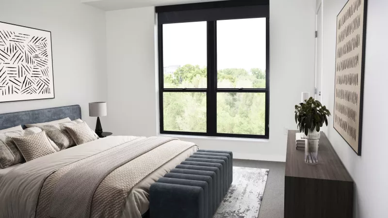 Stylish bedroom with a large bed, blue bench, and expansive window overlooking green trees. Abstract art adorns the walls.