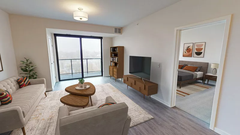 Bright, modern living room with light sofa, wooden furniture, and balcony access. A cozy bedroom is visible through an open doorway.