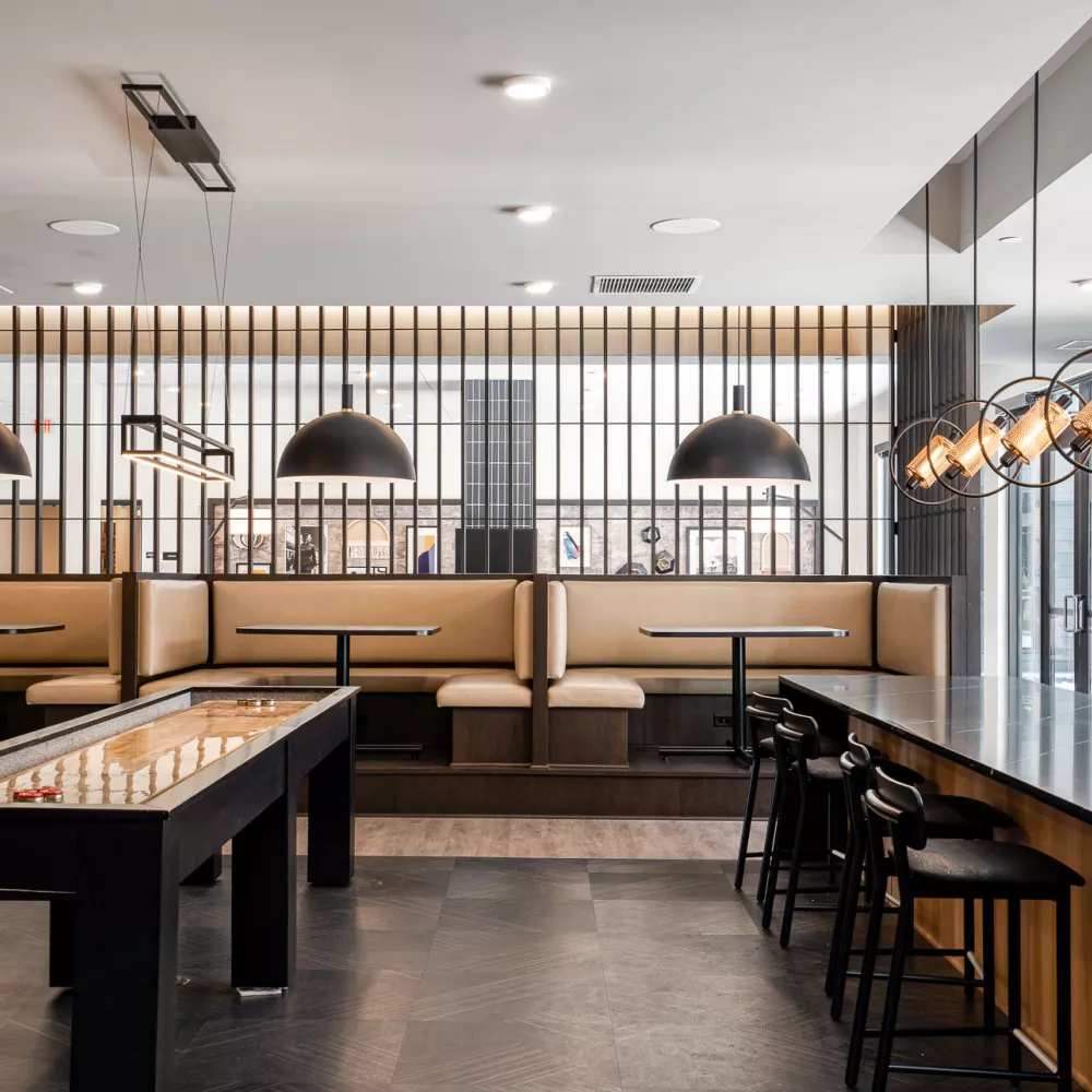 Modern recreational room with shuffleboard, dark counter with stools, and light brown booths under stylish pendant lights.