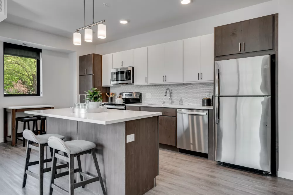 Modern kitchen with a white island, two bar stools, light and dark wood cabinets, and stainless steel appliances.